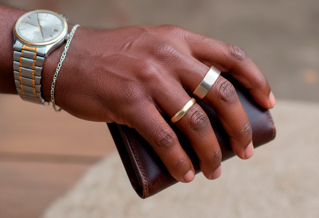 Black man’s hand with gold and silver rings, mixed-metal watch, holding wallet